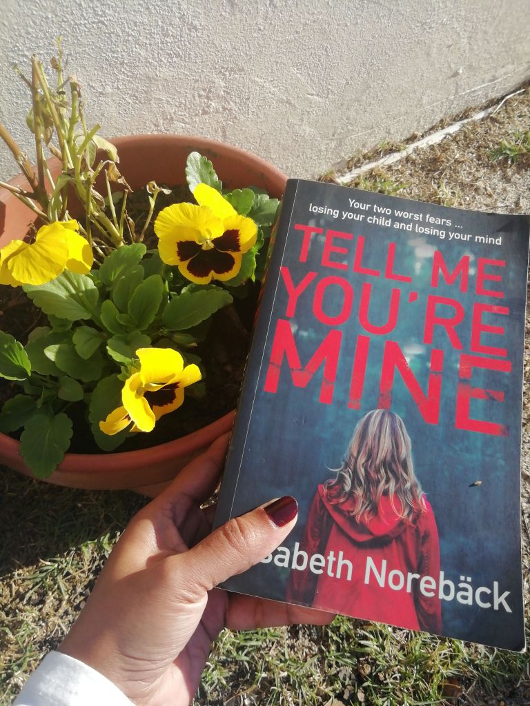 woman's painted thumb nail and finger holding a psychological thriller with a girl in red jacket on the book cover